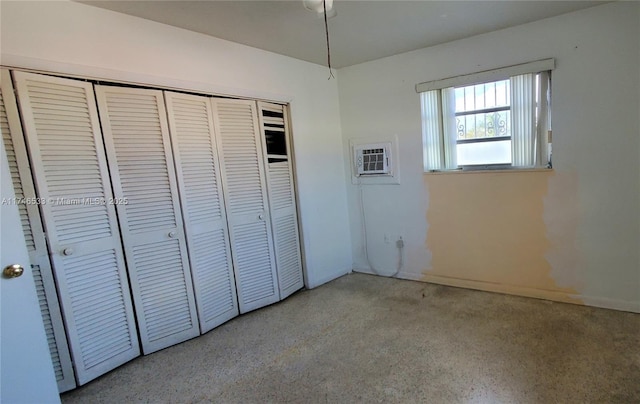 unfurnished bedroom featuring an AC wall unit, speckled floor, and a closet