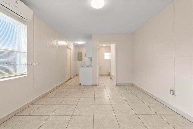 unfurnished room featuring washer / clothes dryer, a wall unit AC, light tile patterned flooring, and a healthy amount of sunlight