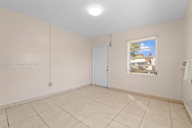 empty room with light tile patterned floors, a wall mounted AC, and baseboards