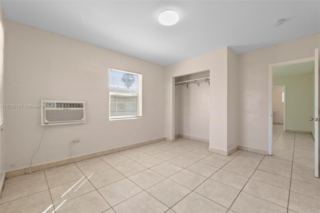 unfurnished bedroom featuring light tile patterned floors, baseboards, a closet, and a wall mounted air conditioner