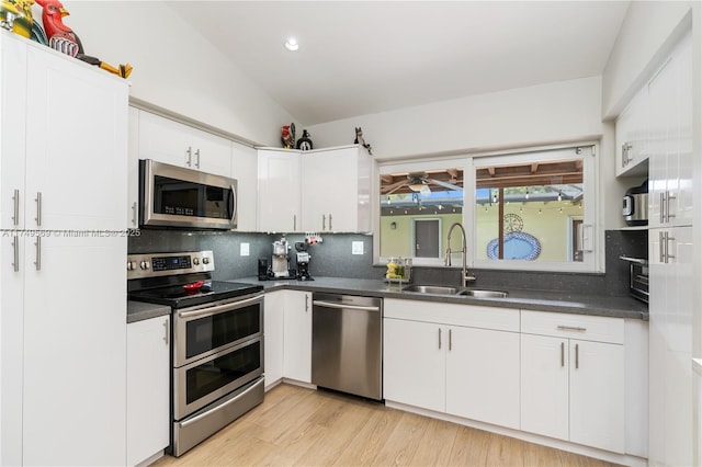 kitchen with appliances with stainless steel finishes, dark countertops, a sink, and lofted ceiling