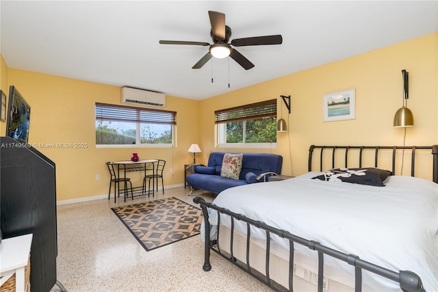 bedroom with a wall mounted air conditioner, ceiling fan, baseboards, and speckled floor