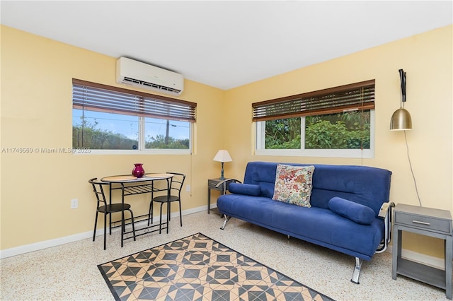 living room with a wall unit AC, plenty of natural light, baseboards, and speckled floor