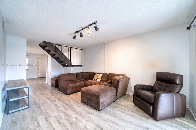 living area with a textured ceiling, track lighting, light wood-type flooring, and baseboards