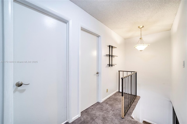 corridor with a textured ceiling, carpet, an upstairs landing, and baseboards