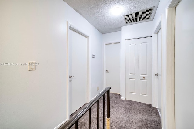 hall featuring carpet, visible vents, and a textured ceiling