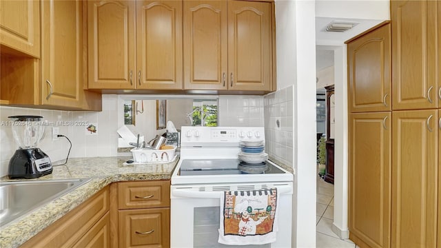 kitchen with light tile patterned floors, light stone counters, white range with electric cooktop, and backsplash