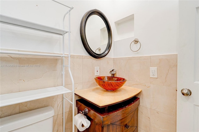 bathroom with toilet, a wainscoted wall, tile walls, and vanity