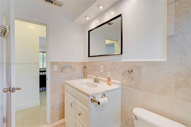 half bathroom with tile patterned flooring, toilet, vanity, visible vents, and tile walls