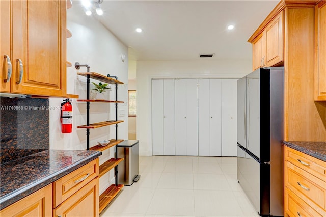 kitchen with visible vents, backsplash, freestanding refrigerator, light tile patterned flooring, and dark stone countertops