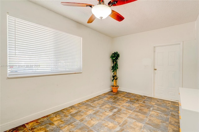 empty room with stone finish floor, a ceiling fan, baseboards, and a textured ceiling