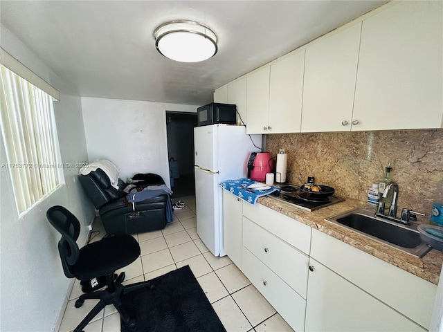 kitchen featuring black microwave, electric stovetop, a sink, freestanding refrigerator, and tasteful backsplash