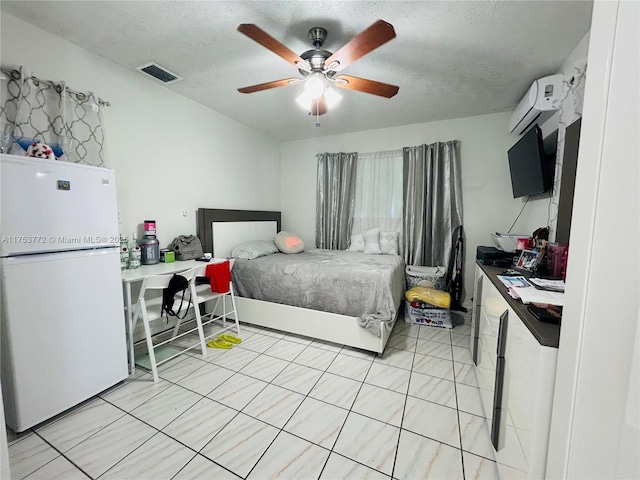 bedroom with a textured ceiling, visible vents, a ceiling fan, freestanding refrigerator, and a wall mounted air conditioner