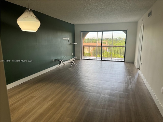 unfurnished room with baseboards, a textured ceiling, visible vents, and wood finished floors