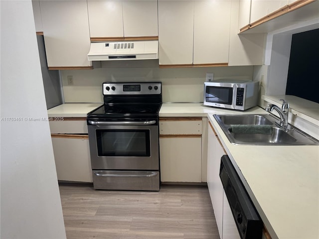 kitchen with under cabinet range hood, a sink, light countertops, appliances with stainless steel finishes, and light wood finished floors