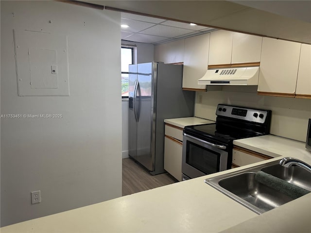 kitchen with a drop ceiling, stainless steel appliances, a sink, exhaust hood, and electric panel