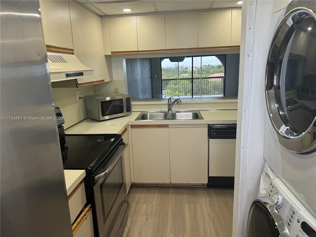 kitchen with stacked washer and clothes dryer, light countertops, appliances with stainless steel finishes, a sink, and exhaust hood