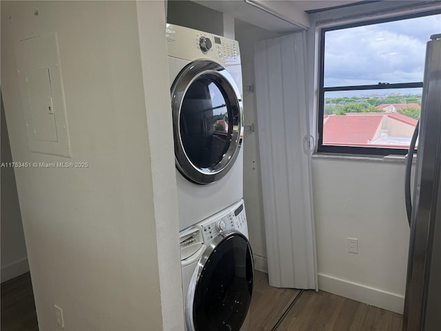 washroom with stacked washer and clothes dryer, wood finished floors, laundry area, electric panel, and baseboards