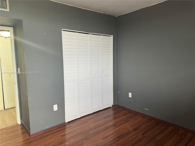 unfurnished bedroom with a closet, wood finished floors, visible vents, and baseboards