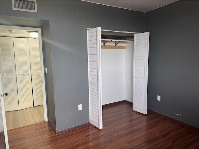 unfurnished bedroom featuring a closet, visible vents, baseboards, and wood finished floors