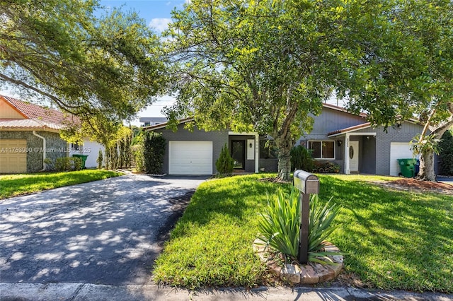 view of property hidden behind natural elements with aphalt driveway, brick siding, an attached garage, and a front lawn