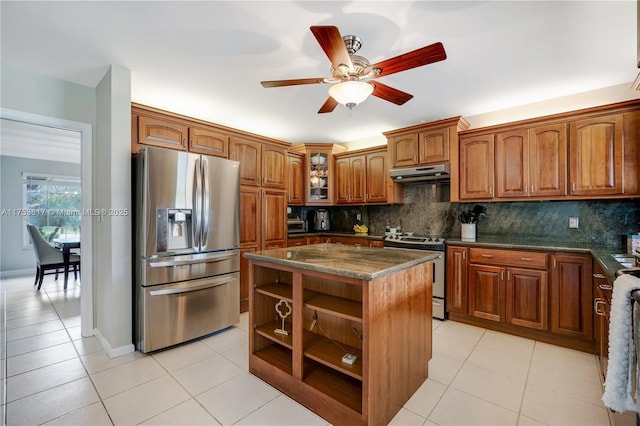 kitchen with light tile patterned floors, under cabinet range hood, stainless steel appliances, backsplash, and brown cabinets