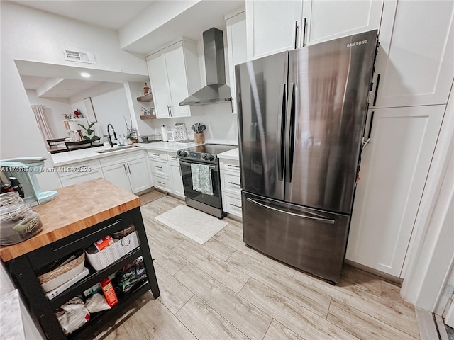 kitchen featuring black electric range, visible vents, freestanding refrigerator, a sink, and wall chimney range hood