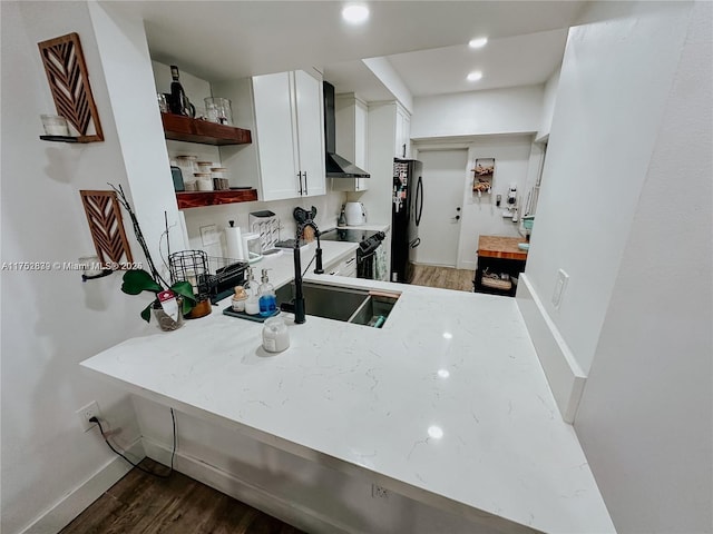 kitchen featuring freestanding refrigerator, wood finished floors, wall chimney range hood, and open shelves