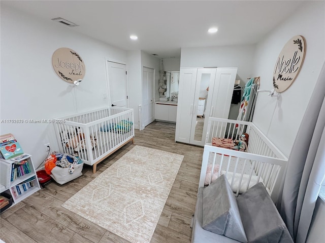 bedroom with a nursery area, wood finished floors, visible vents, and recessed lighting