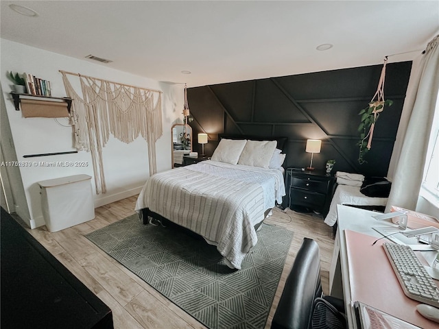 bedroom with light wood-style floors, visible vents, and a decorative wall