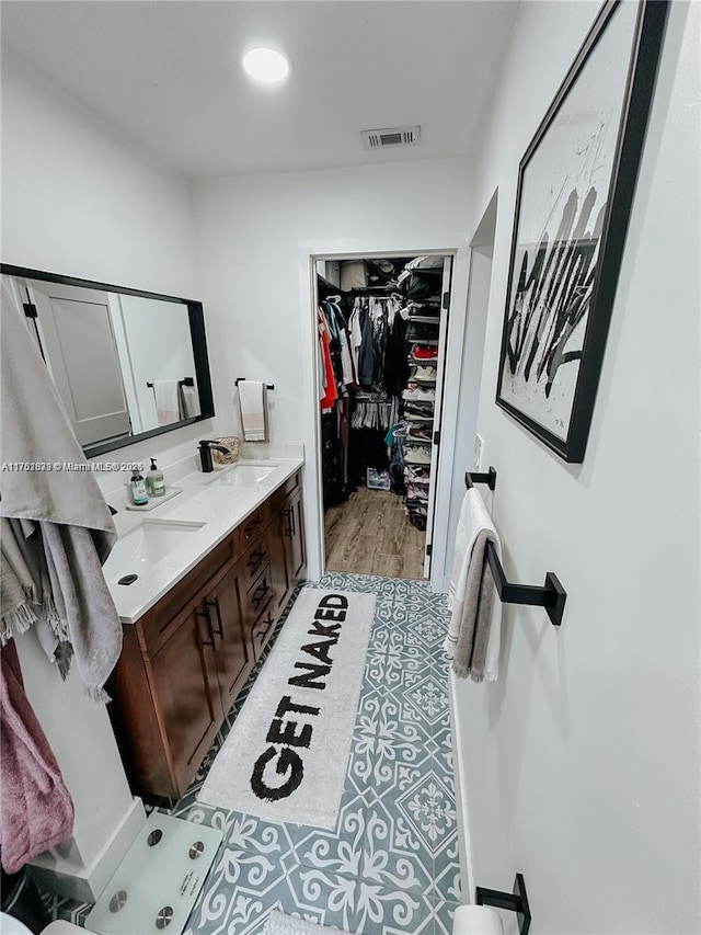 full bath featuring double vanity, a spacious closet, visible vents, and a sink