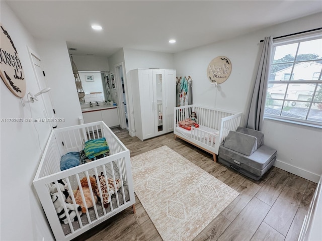 bedroom with a nursery area, baseboards, wood finished floors, and recessed lighting