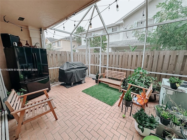 view of patio with glass enclosure, a grill, and fence