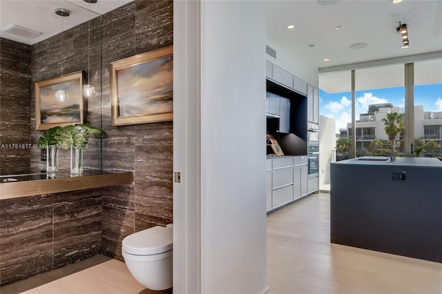 bathroom with visible vents, toilet, wood finished floors, expansive windows, and a sink