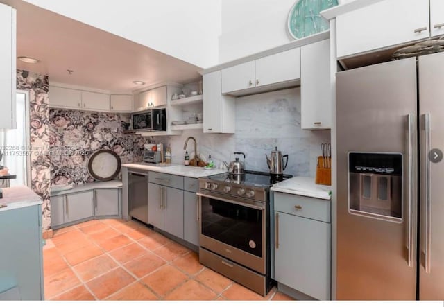 kitchen featuring light countertops, appliances with stainless steel finishes, gray cabinets, decorative backsplash, and open shelves