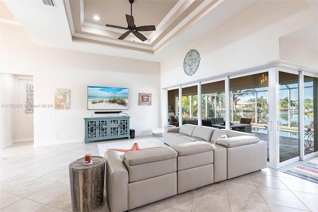 living room featuring a tray ceiling, light tile patterned floors, a towering ceiling, a ceiling fan, and ornamental molding