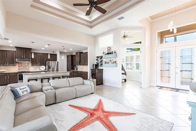 living room featuring visible vents, a high ceiling, a tray ceiling, crown molding, and light tile patterned flooring