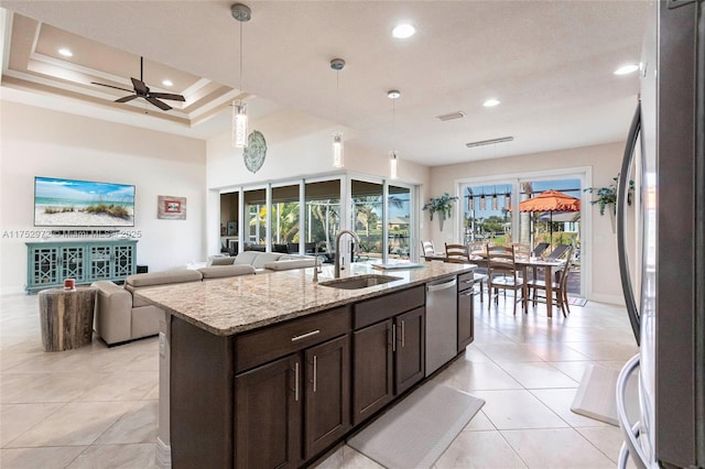 kitchen with appliances with stainless steel finishes, open floor plan, light stone countertops, dark brown cabinets, and a sink