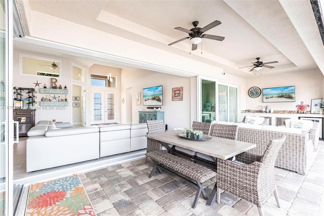 sunroom featuring a healthy amount of sunlight, ceiling fan, a raised ceiling, and french doors