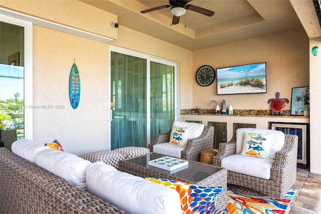 living area with beverage cooler, ceiling fan, and a tray ceiling