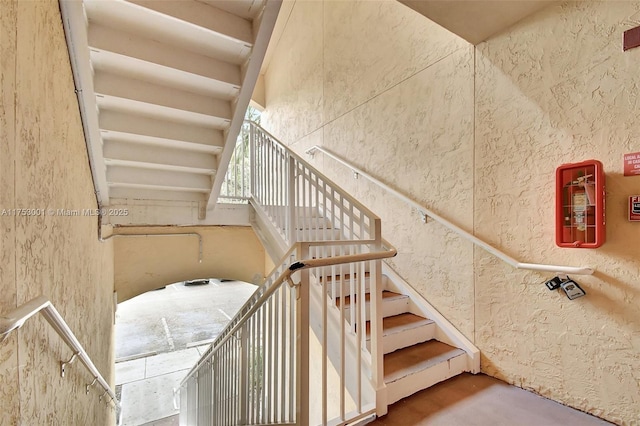 staircase featuring concrete flooring and a textured wall