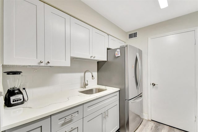 kitchen featuring light stone counters, a sink, visible vents, backsplash, and freestanding refrigerator