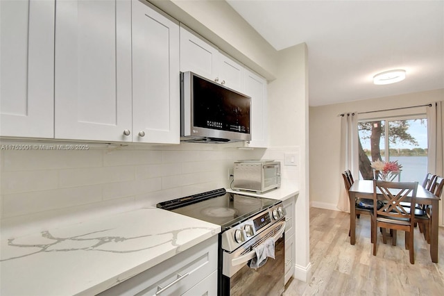 kitchen with tasteful backsplash, appliances with stainless steel finishes, light stone countertops, light wood-type flooring, and white cabinetry