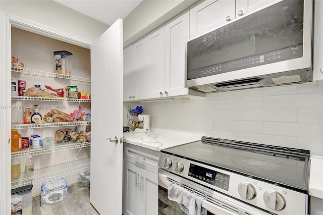 kitchen with tasteful backsplash, white cabinets, appliances with stainless steel finishes, light stone counters, and wood finished floors