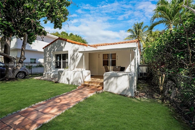 view of front of home with a tiled roof, a front yard, fence, and stucco siding