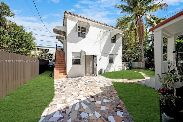 rear view of house featuring a lawn, a patio, a tiled roof, fence, and stucco siding