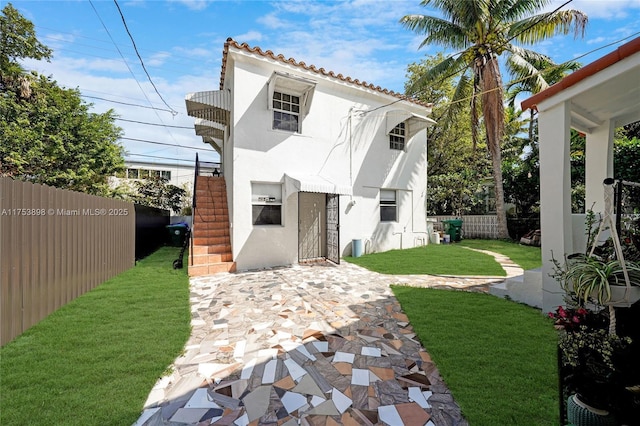 back of property with a tile roof, a yard, stucco siding, and fence
