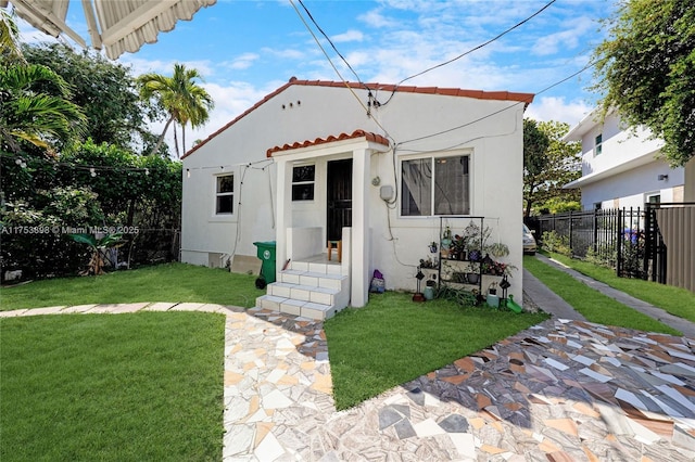 mediterranean / spanish-style house with a tile roof, a front lawn, stucco siding, and fence