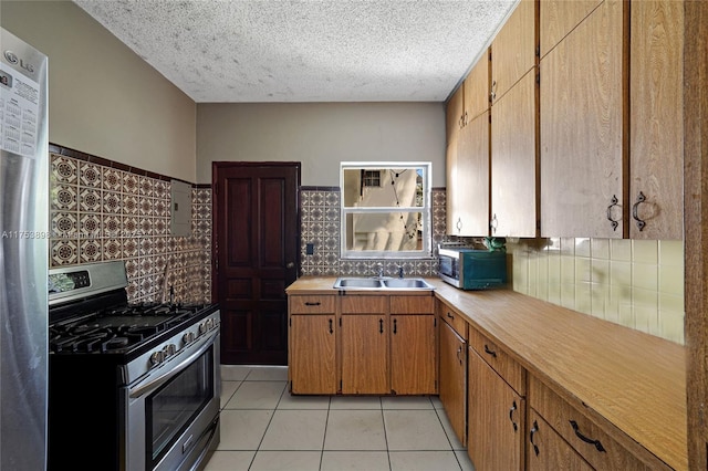 kitchen with light tile patterned floors, appliances with stainless steel finishes, light countertops, a textured ceiling, and a sink