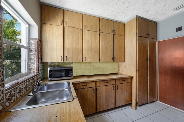 kitchen featuring light tile patterned floors, tasteful backsplash, visible vents, stainless steel microwave, and a sink